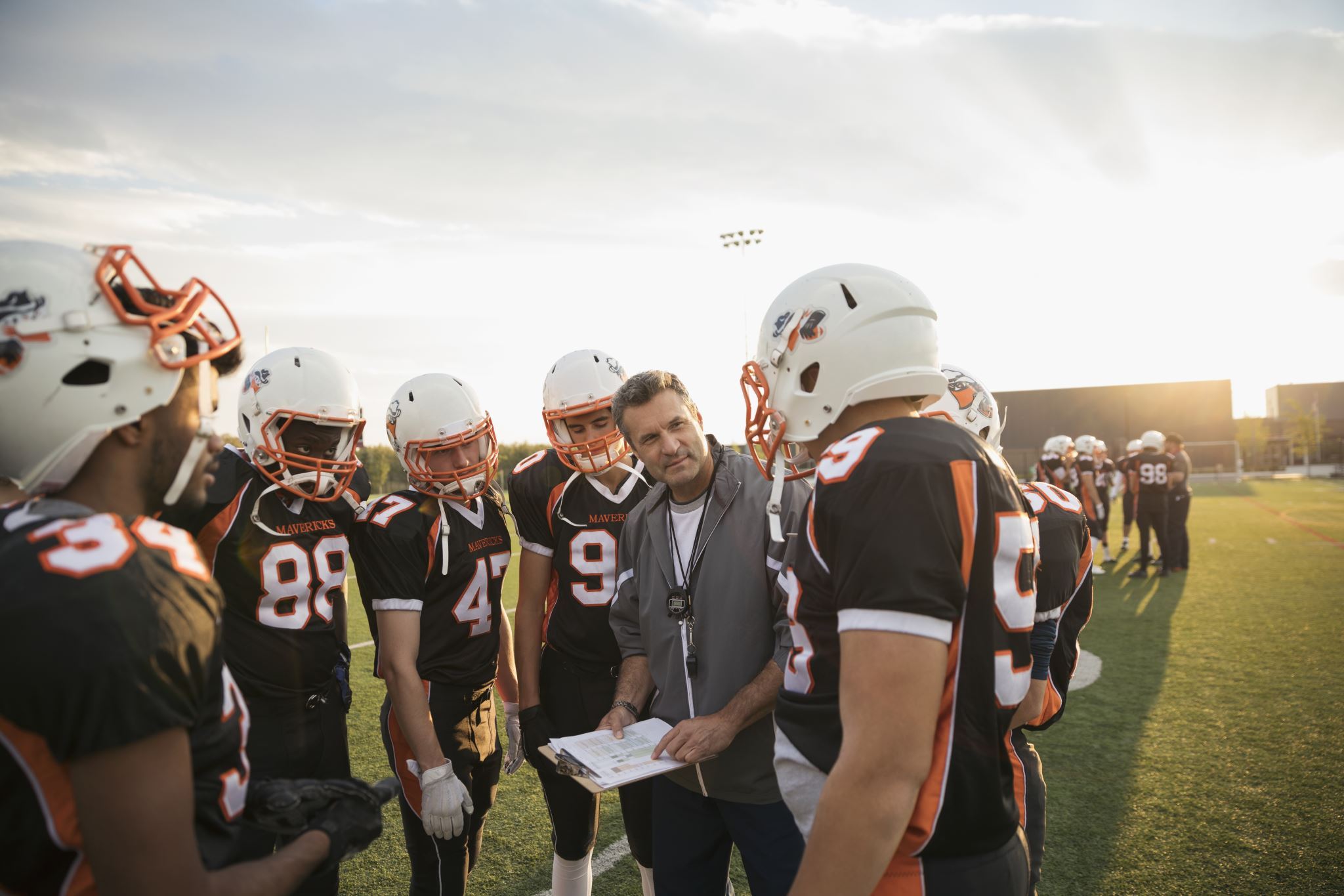 Trainer-met-een-klembord-die-tegen-een-footballteam-praat-in-een-huddle-op-het-veld